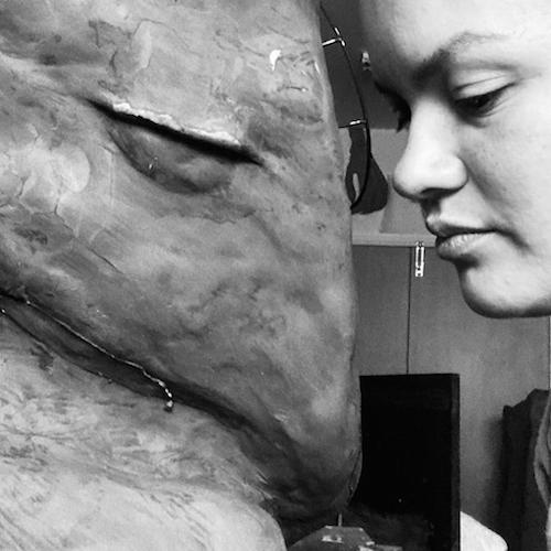 A black and white photograph of artist Fani Parali face to face with her sculpture of a harpy eagle.