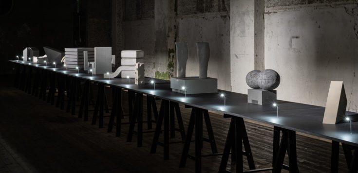 Multiple jesmonite cultural buildings in a line, lit with small street lights on a black trestle table.⠀
