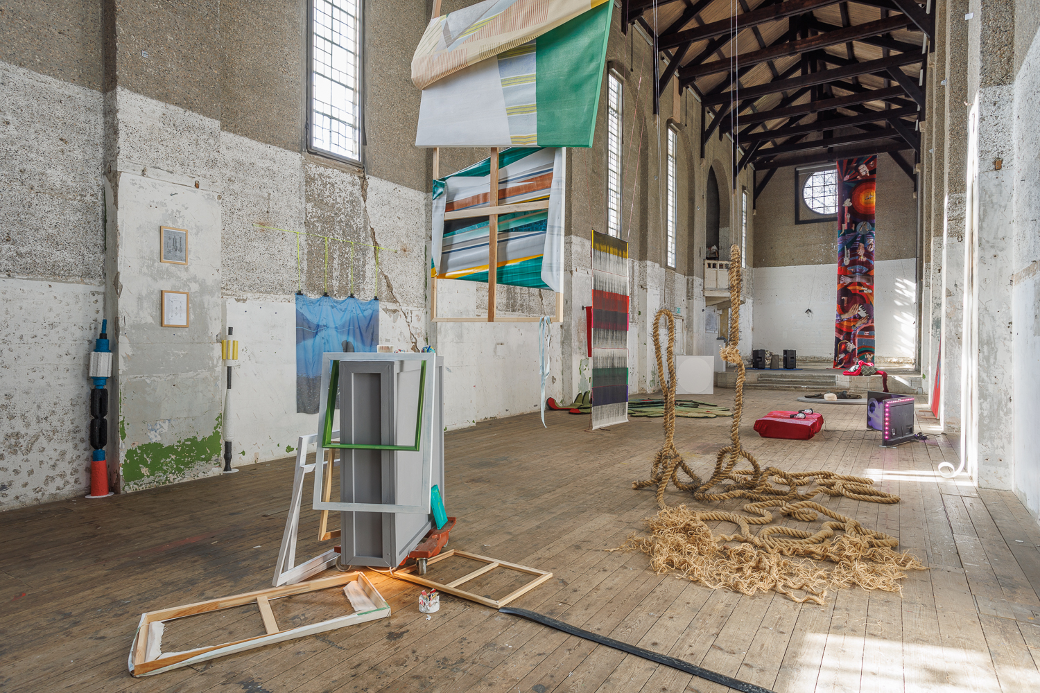 A collection of sculptures, some hanging, some placed on the floor occupy the gallery space, an old concrete church.