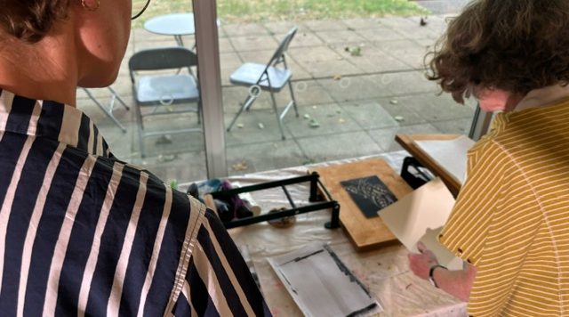 Two senior art students engage in a lino printing project, working together on a piece of paper at a table.